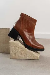 Botinetas de cuero vacuno con textura tipo reptil en color marrón chocolate. Presentan un diseño de caña media con cierre posterior, puntera redondeada y suela de goma con taco cuadrado robusto.