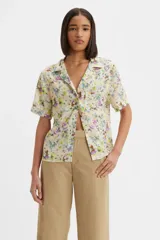 Camisa de manga corta con cuello tipo solapa y cierre frontal de botones. Presenta un estampado floral multicolor sobre fondo claro, corte recto y un bolsillo frontal en el pecho con etiqueta de marca.