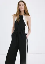 Jardinera larga de lino y viscosa, color negro con detalles de rayas blancas en contraste en los laterales. Cuenta con cuello halter, diseño sin mangas, dos bolsillos laterales y detalle de lazo ajustable en la cintura.