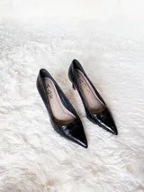 Zapatos de tacón alto con textura de reptil, color negro, con suela roja característica.