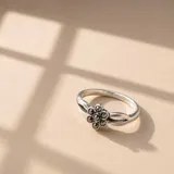 Anillo de plata 925 con diseño de flor central compuesta por pequeñas piedras oscuras engastadas. La banda presenta un diseño entrelazado en los laterales.