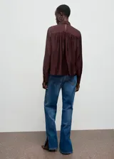 Blusa de cuello alto con detalle de fular integrado, confeccionada en tejido con textura. Presenta diseño recto, manga larga con puños abotonados y cierre posterior.
