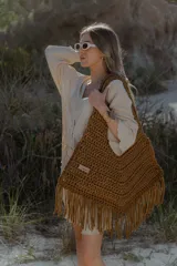 Bolso de mano grande tejido a crochet con técnica de trapillo reciclado, color beige visón. Presenta un diseño de punto grueso y flecos largos en el borde inferior.