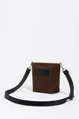 Bolso bandolera de gabardina color marrón, con diseño compacto, cierre de cremallera y asa de tejido ajustable. Presenta el logo de la marca aplicado en la parte frontal.