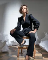 Mono largo negro de acetato con mangas largas abullonadas con elástico en los puños, detalle de raso en hombros y cinturón, escote en V regulable con cierre invisible y textura plisada artesanal en el frente superior.