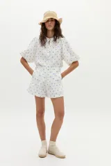 Short de tiro alto confeccionado en lino blanco con estampado de lunares azules. Presenta pinzas frontales y cierre con botones.