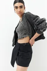 Minifalda negra de jean asimétrica con bolsillos de solapa y tiras ajustables con hebillas en los laterales.