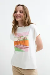 Remera de manga corta color blanco, confeccionada en 100% algodón, con cuello redondo y diseño gráfico frontal estilo paisaje tropical con palmeras en tonos rosado, naranja y verde.
