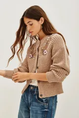 Cardigan de punto grueso en color azul, con cierre frontal de botones, mangas largas con puños de encaje blanco y detalle de bordado floral con pedrería brillante en el pecho.