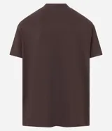 Remera de algodón peruano color marrón oscuro, corte comfort, con cuello redondo y mangas cortas. Presenta un pequeño parche rectangular estampado en el pecho con texto en tonos naranja y blanco.