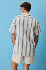Camisa de manga corta a rayas verticales en tonos azul y blanco, con cuello camisero, cierre frontal de botones y un bolsillo en el pecho con etiqueta aplicada.