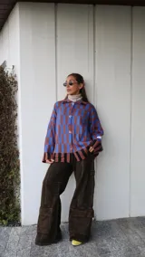 Buzo tipo saco abotonado con diseño de cuadros en tonos marrones y beige, corte recto y oversize. Presenta cuello camisero, cierre frontal con botones personalizados y dos bolsillos delanteros.