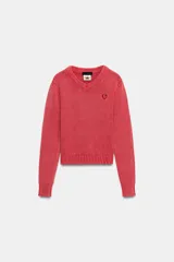 Jersey de punto de algodón color rosado, con cuello en V, manga larga y acabados en rib. Presenta un pequeño parche gráfico bordado en el pecho.