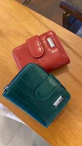 Billetera corta de símil cuero con textura croco, cierre perimetral y solapa con broche a presión. Cuenta con tarjeteros, visor, compartimento para billetes y bolsillo posterior con cierre.