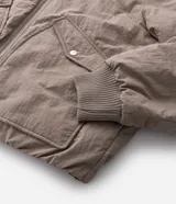Campera bomber masculina de poliamida, con cuello, puños y ruedo de tejido elástico. Presenta cierre frontal con cremallera, dos bolsillos laterales con solapa y botón, y un pequeño bolsillo con cierre en una de las mangas.