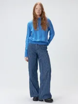 Sweater de punto con diseño de rayas verticales en tonos negro y gris oscuro. Presenta cuello alto tipo polera, mangas largas con puños ajustados y ruedo elástico. Incluye un pequeño bordado en color rojo en el pecho.