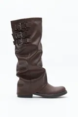 Bota de caña alta color marrón, con diseño utilitario y estructura flexible. Presenta puntera redondeada, taco bajo y detalle de tres hebillas metálicas en la parte superior.