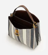Cartera bucket pequeña de Satinato con diseño de rayas verticales en tonos blanco, azul marino y beige, confeccionada en tejido estructurado. Cuenta con asa de mano fija, asa larga desmontable de cuero sintético marrón, detalles de herrajes metálicos dorados, argolla metálica colgante en el frente y cierre superior.
