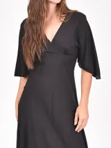 Vestido largo negro de corte evasé, con escote en V cruzado y mangas tres cuartos acampanadas.