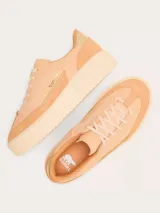 Championes Sorel modelo Ona Ave T-Toe, color beige con detalles en gamuza y cuero. Presenta suela de plataforma con diseño estriado y detalle metálico dorado en el talón.