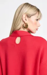 Blusa de punto color rojo con diseño de cuello asimétrico que incorpora una bufanda integrada. Presenta mangas anchas de largo tres cuartos y un corte holgado.
