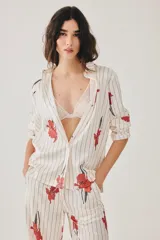 Pijama de satén compuesto por una camisa de manga larga con botones y un pantalón largo, ambos de color crudo con estampado de rayas verticales negras y flores rojas.