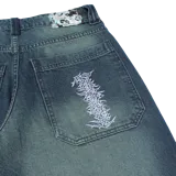 Pantalón de jean azul con efecto lavado y teñido verdoso, de corte amplio y tiro medio.