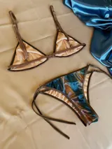 Conjunto de bikini confeccionado en terciopelo con efecto degradado en tonos azul, marrón y rosado. El corpiño es de estilo triangular con aros metálicos decorativos en el centro y breteles regulables. La bombacha es de corte clásico con laterales ajustables mediante tiras.