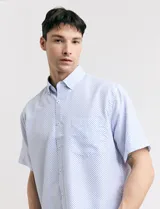 Camisa blanca con estampado de micro lunares celestes, de corte clásico, manga corta, cuello abotonado y bolsillo en el pecho.