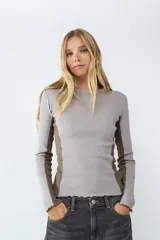 Remera de manga larga en tejido jersey, con diseño de bloques de color en tonos gris y marrón. Presenta un calce ajustado, cuello redondo y terminaciones con borde ondulado.