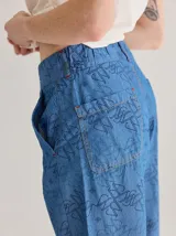 Pantalón de jean de corte ancho y tiro medio, con estampado de monograma en color azul oscuro sobre base de denim azul claro. Presenta cierre frontal con botón y costuras a la vista.