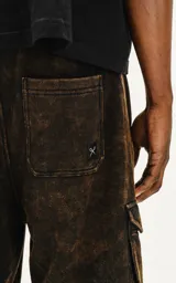 Bermuda cargo de algodón rústico, color marrón oscuro con efecto desgastado (acid wash/oxidado). Presenta un calce oversize, cintura elástica y grandes bolsillos laterales con tapa.