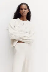 Pantalón de punto suave color beige, de tiro alto con cintura elástica, perneras rectas, secciones laterales con diseño pointelle y detalle de volados en el bajo.