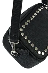 Bandolera color beige con textura granulada, adornada con remaches metálicos plateados en el frente. Cuenta con cierre superior y correa ajustable.