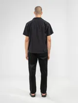 Camisa negra de manga corta con cuello camp y calce relajado. Confeccionada en una mezcla de lino y algodón, terminada con botones de madera y parche característico de Polonio. Hecha en Italia.