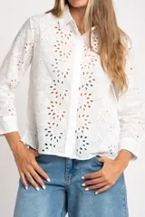 Blusa blanca de manga larga con cuello camisero y bordado tipo broderie anglaise con diseño floral calado.