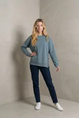 Buzo de calce relajado con cuello redondo y mangas largas. Presenta aberturas laterales con botones funcionales que permiten regular la caída de la prenda.