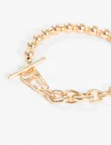 Pulsera dorada con eslabones irregulares y cierre de barra en forma de T.