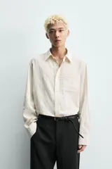 Camisa de corte relajado confeccionada en tejido fluido con textura jacquard de rayas verticales. Presenta cuello clásico, cierre frontal con botones, manga larga con puños abotonados y un bolsillo de parche en el pecho.