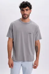 Remera gris claro de manga corta, con cuello redondo y estampa sutil con la inscripción "Athletics" en el pecho.