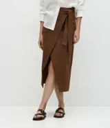 Pollera midi envolvente color marrón, de corte evasé confeccionada en sarga de algodón, con cinturón con lazo en la cintura y diseño cruzado con abertura delantera.
