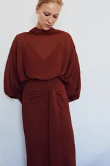 Vestido largo fluido en color bordó, confeccionado en georgette. Presenta cuello redondo, mangas largas con pliegues terminadas en puños y tiras ajustables para atar en la cintura. Incluye forro interior a tono.