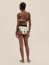 Bikini de dos piezas con estampado de lunares negros sobre fondo blanco. El corpiño es de corte triangular con tirantes finos y se ata en la espalda. La bombacha es de corte alto a la cintura con una banda ancha negra.