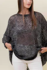 Buzo de tejido liviano y calado con brillo sutil, color gris oscuro o negro. Presenta un calce amplio y mangas amplias, con un detalle de tiras entrelazadas en la espalda. El largo es irregular, más largo en la parte trasera.