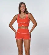Conjunto deportivo de dos piezas color naranja, compuesto por un top de escote redondo con costuras a la vista en contraste y un short de tiro alto con costuras a la vista. El top presenta el logo de la marca estampado en el frente.