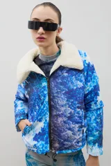 Campera con estampado de bosque en tonos azules, cuello de sherpa en color crema y cierre frontal con cremallera. Cuenta con elástico ajustable en la cintura.