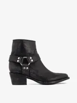 Bota corta de cuero negro con punta estilizada y taco bajo. Presenta un detalle de arnés desmontable alrededor del tobillo con argolla metálica y tachas plateadas.