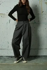 Pantalón de corte holgado y tiro alto en color gris oscuro, con pinzas frontales y costuras verticales decorativas a lo largo de las piernas.