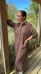 Vestido camisero largo de lino blanco, con cuello camisero, manga corta enrollada y cierre frontal de botones de nácar. Presenta aberturas laterales en el bajo.