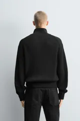 Chaqueta de punto perlado con lana, de corte relajado, cuello subido y cierre frontal con cremallera de doble dirección. Presenta mangas largas y acabados en rib en puños y ruedo.